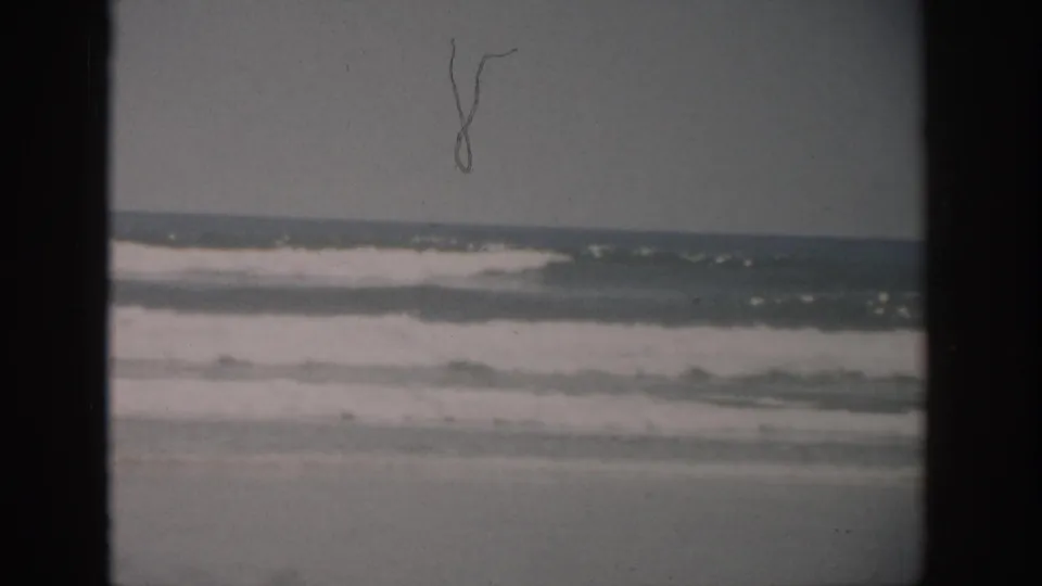 1959 Florida 8mm frame showing white surf rolling toward wet sand under an overcast horizon.