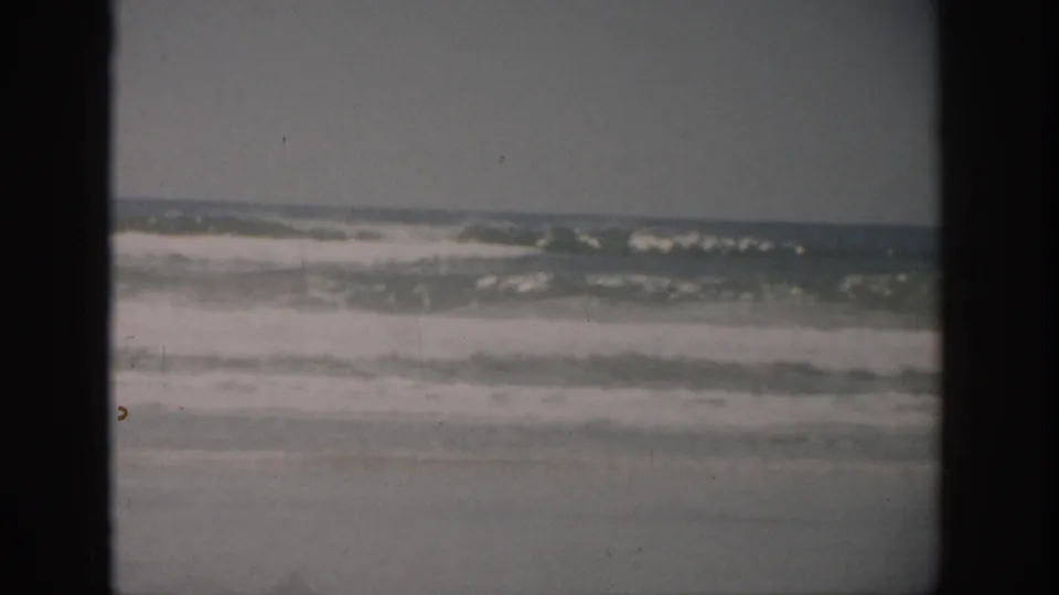 1959 Florida home-movie frame with choppy waves, white foam, and dark 8mm gate borders.