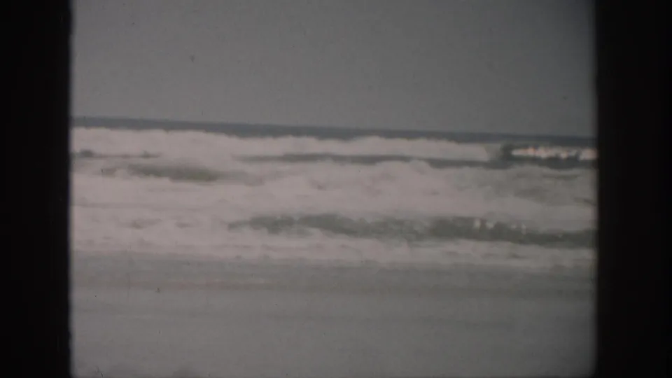 Vintage 8mm Florida beach frame showing foamy surf washing toward shore under muted light.