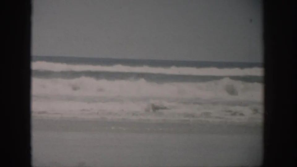 1959 Florida coastal frame with low surf, white foam, and visible 8mm film border texture.