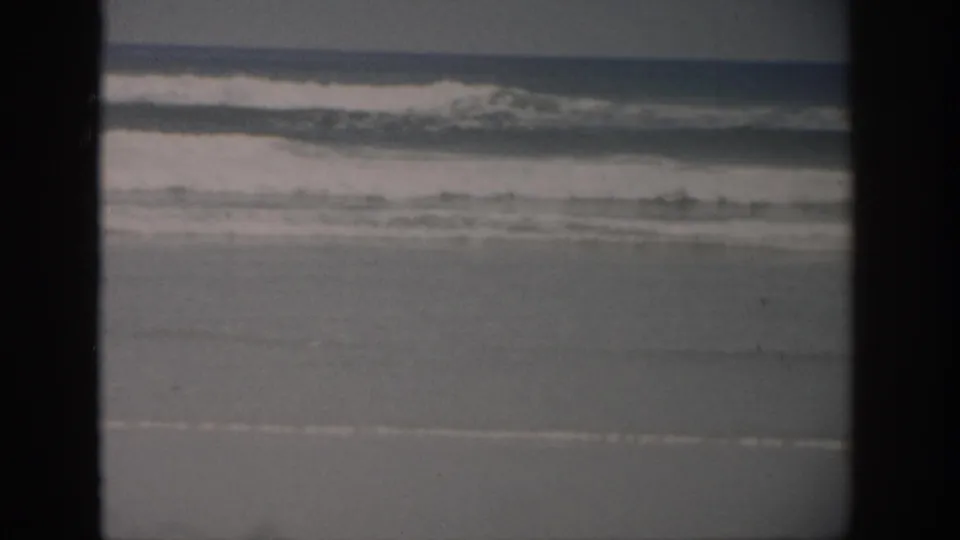 Faded 1959 Florida 8mm view of an empty beach, shallow surf, and flat horizon, framed by dark scan borders.