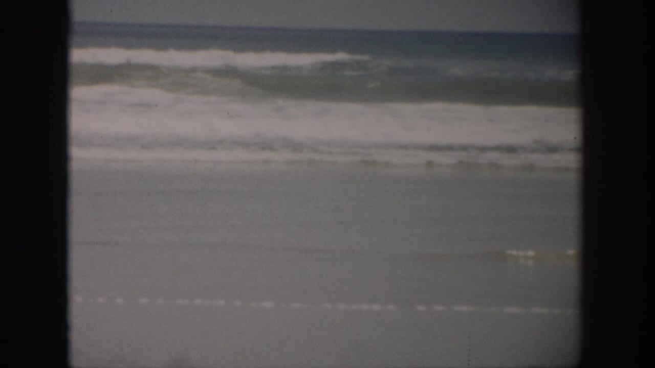 1959 Florida 8mm frame showing ocean surf approaching a broad, wet sandy shoreline with dark film borders.