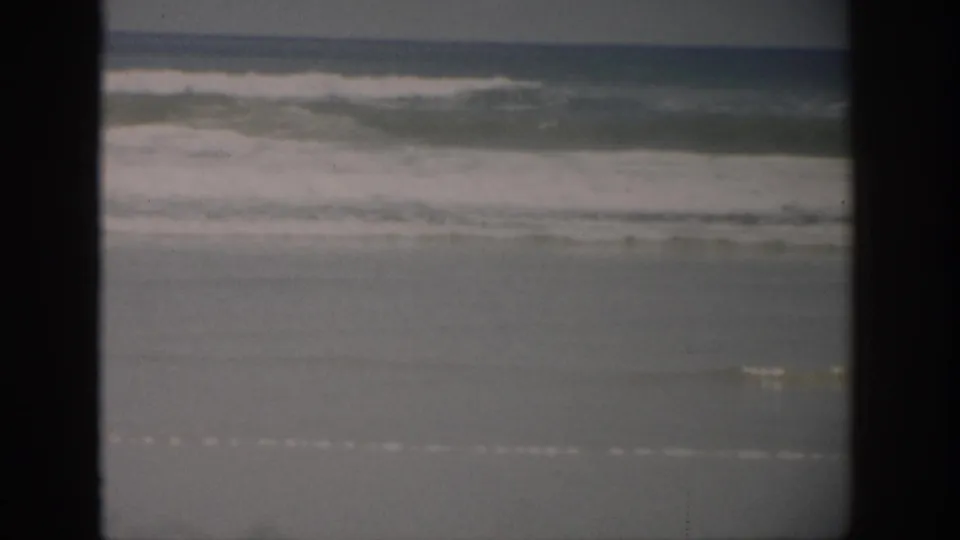 1959 Florida 8mm frame showing ocean surf approaching a broad, wet sandy shoreline with dark film borders.