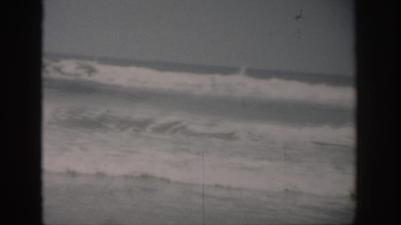 1959 Florida 8mm frame of foamy ocean surf rolling in under an overcast sky, with visible film scratches and gate borders.