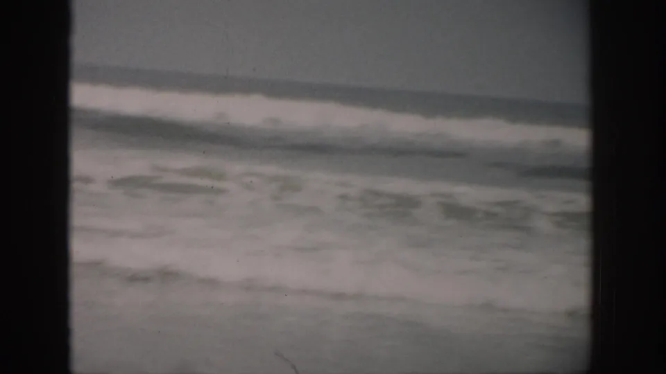 1959 Florida coastal home-movie frame showing low rolling surf and a gray horizon, with dust and scratches visible on the film.