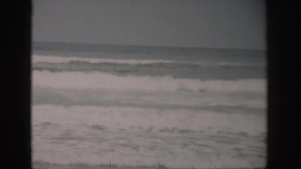 1959 Florida 8mm frame with choppy waves breaking in bands across a subdued shoreline scene.