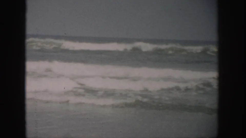 Late-1950s Florida surf view with a breaking wave offshore, white foam in the foreground, and muted overcast light.