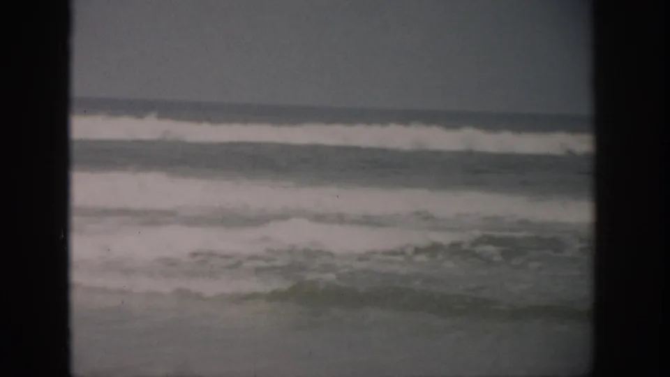 1959 Florida 8mm frame showing small gray waves and white foam under a cloudy sky, bordered by dark film gate edges.