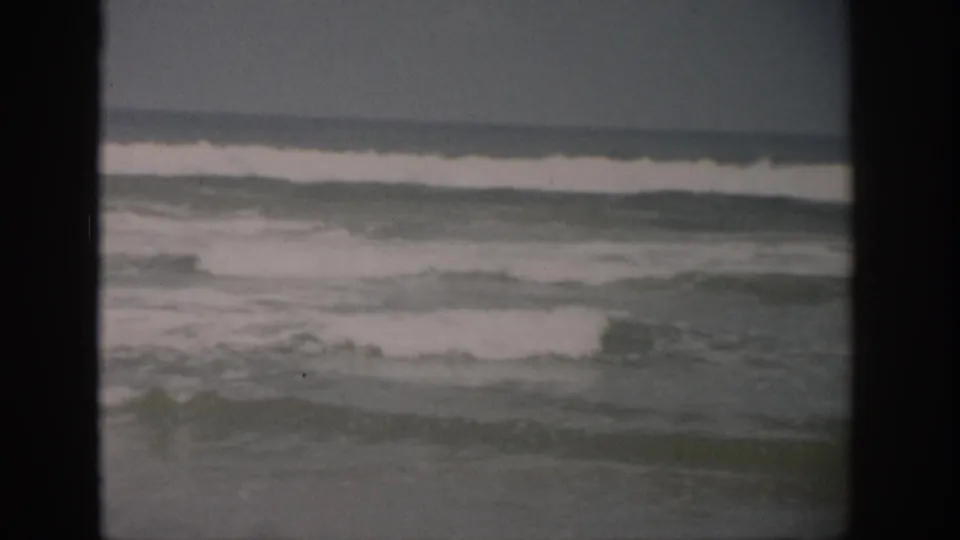 1959 Florida coastal frame with low waves, pale foam, and a soft horizon in faded 8mm color.