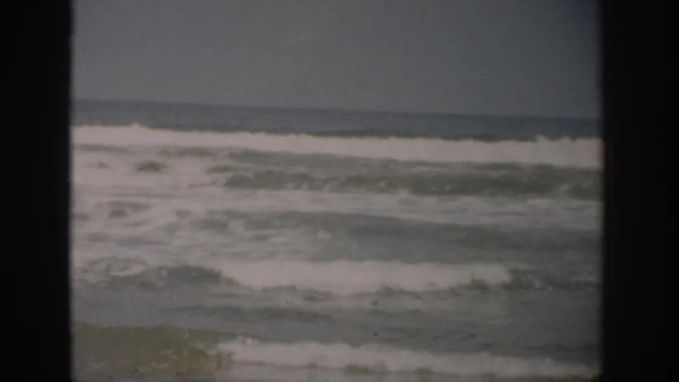1959 Florida 8mm view of foamy surf moving toward a sandy shoreline under an overcast sky.