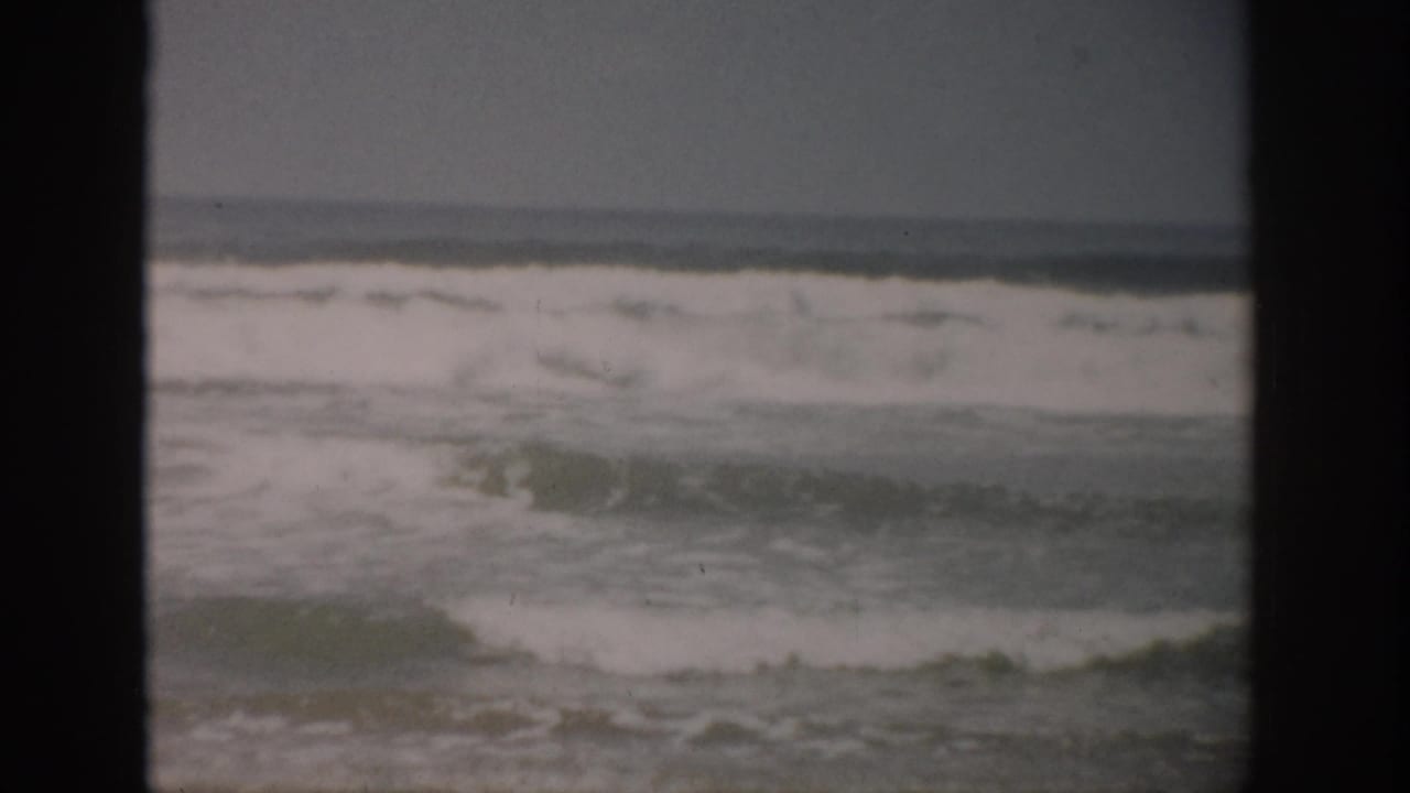 1959 Florida 8mm frame showing surf and sea foam rolling toward an empty shoreline beneath an overcast sky.
