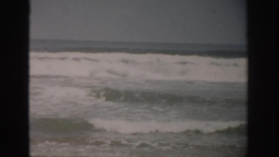 1959 Florida 8mm frame showing surf and sea foam rolling toward an empty shoreline beneath an overcast sky.