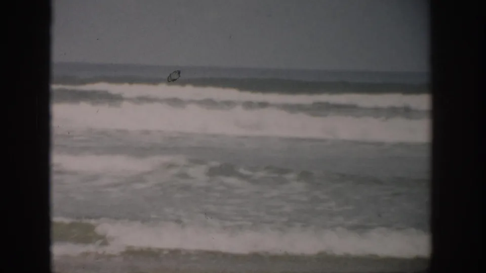 1959 Florida beach footage frame with layered surf, whitecaps, muted color, and dark film gate edges.