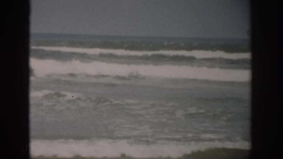 1959 Florida 8mm frame showing foamy waves approaching a quiet, empty beach in faded color.