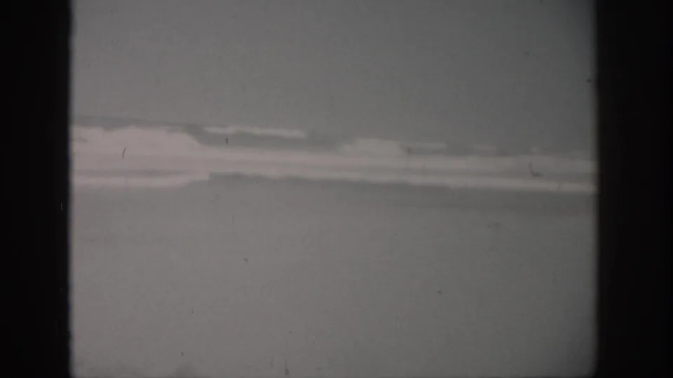 1959 Florida coastal frame with distant waves, pale surf, empty beach, and subdued overcast light.