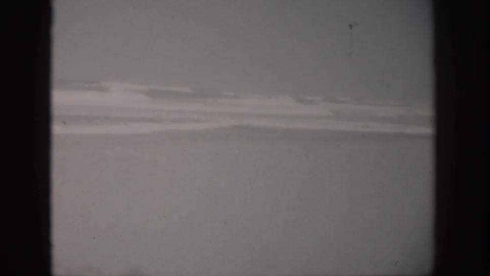 1959 Florida coastal home-movie frame with muted rough water, pale wave foam, and a cloudy evening sky.
