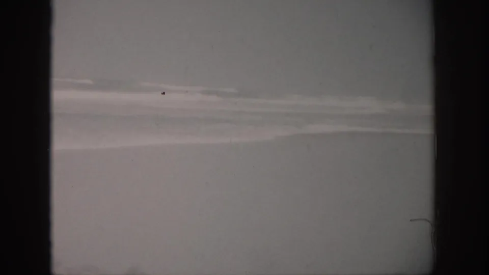 1959 Florida home-movie frame showing a cloudy ocean horizon, pale breaking surf, and visible 8mm scan texture.