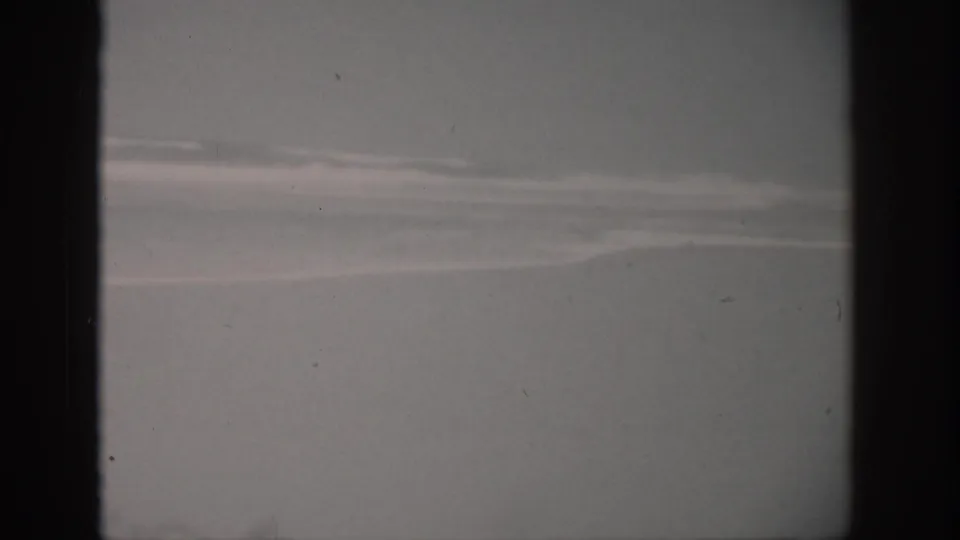 1959 Florida 8mm frame showing pale shoreline and soft surf bands under muted sky, with dark film-edge framing.
