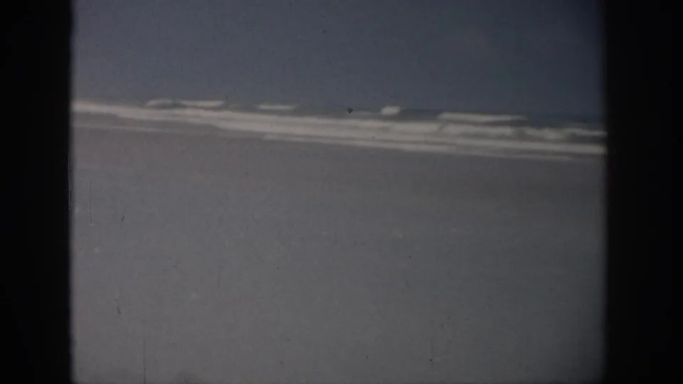 A 1959 Florida coastal view from above, with white surf streaks crossing pale sand and blue-gray water.