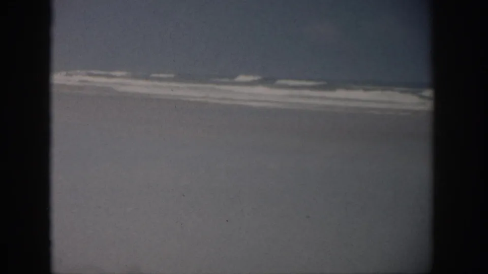 Vintage 8mm Florida shoreline frame with rolling waves, faded color, and heavy dark borders from the film scan.