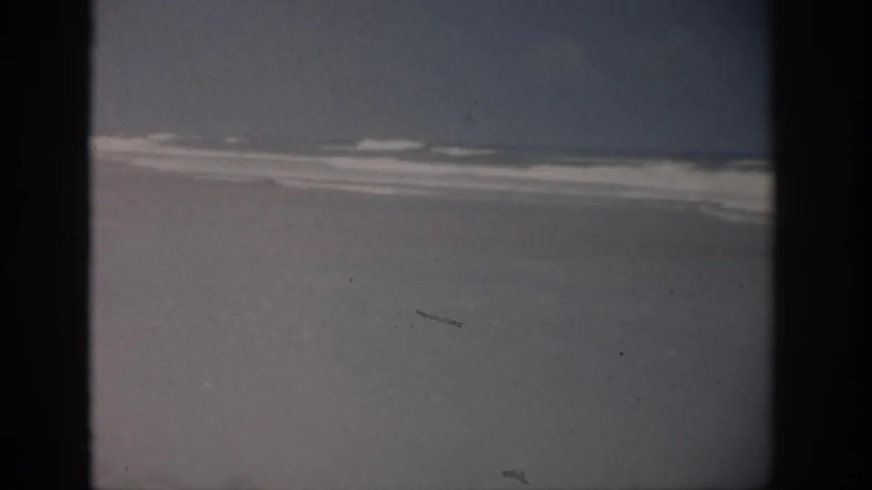 Final 1959 Florida 8mm frame showing a quiet shoreline, low surf, faded color, and small physical-film marks.
