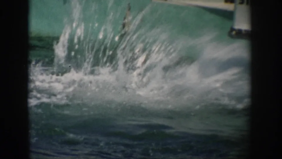 A dolphin show moment in 1959 Florida 8mm footage shows a forceful splash rising from turquoise aquarium tank water.