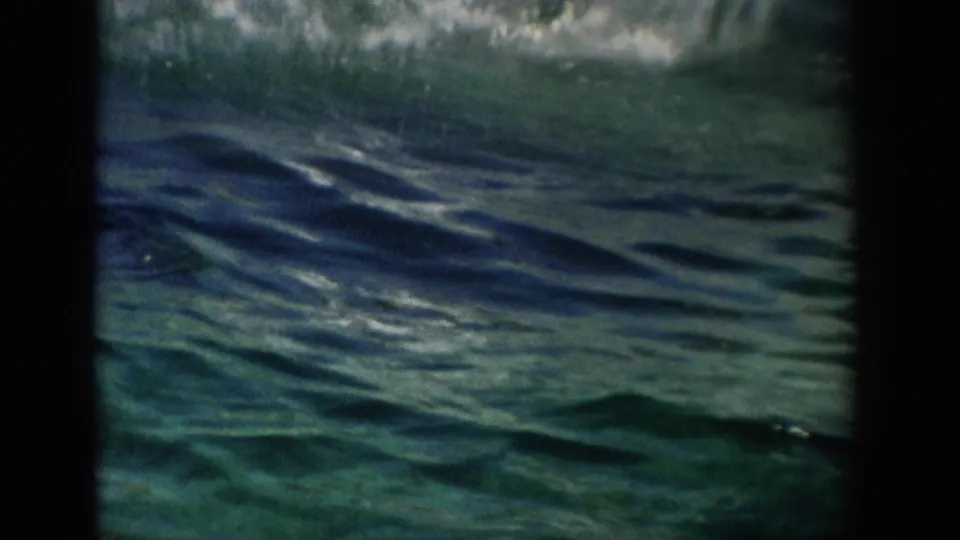 The 8mm frame holds on rippling green-blue aquarium water after the dolphin movement, with foam and soft grain visible.