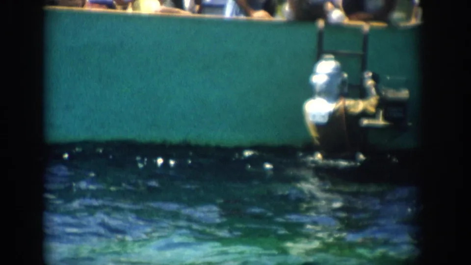 1959 Florida 8mm frame showing the man lower in the exhibit pool beside the ladder, with green wall and rippling water around him.