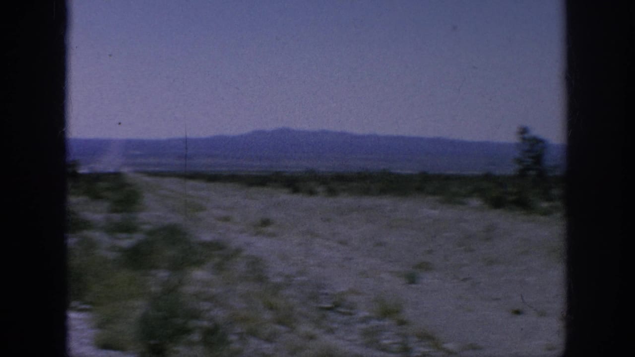 Roadside track through sparse scrub with mountains on the horizon.