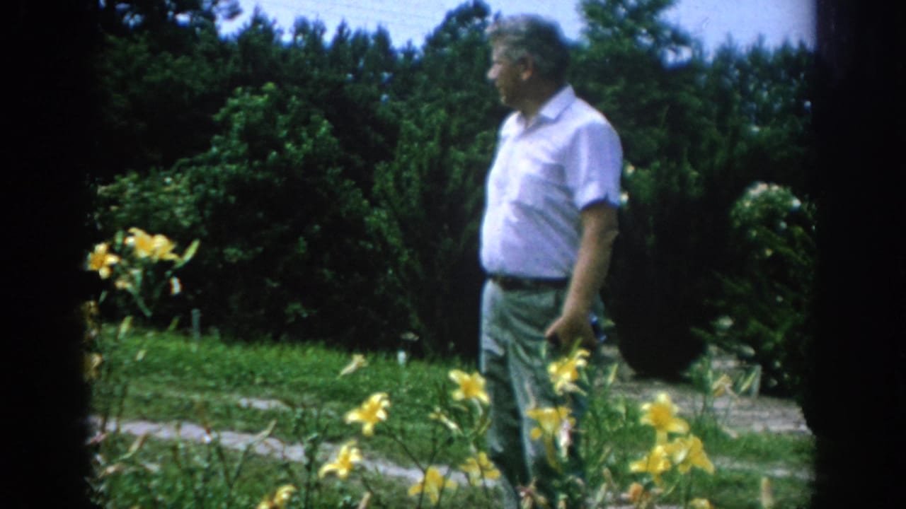 Adult man in a white short-sleeved shirt stands near yellow flowers in a Blainsport, Pennsylvania garden, consistent with 1962 metadata.