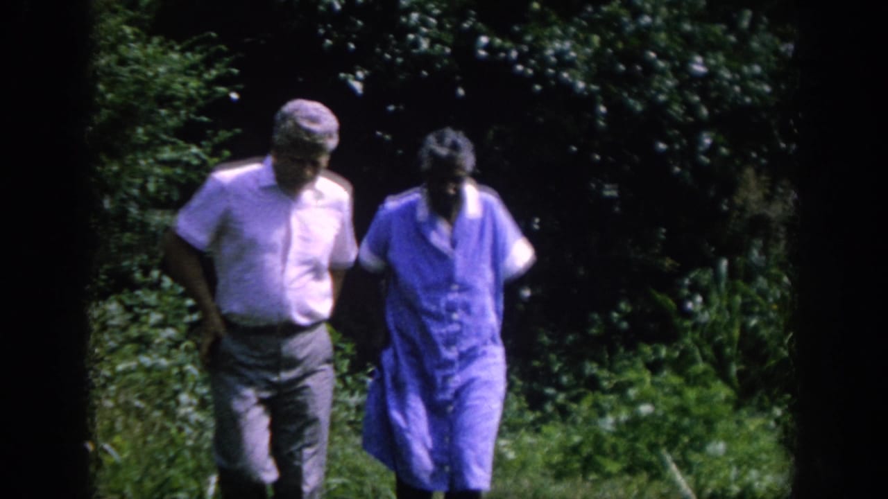 In 1962 Blainsport, Pennsylvania home-movie footage, two adults walk side by side through dense garden foliage.