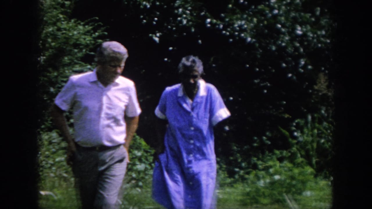 A man and woman continue walking beside dense greenery.