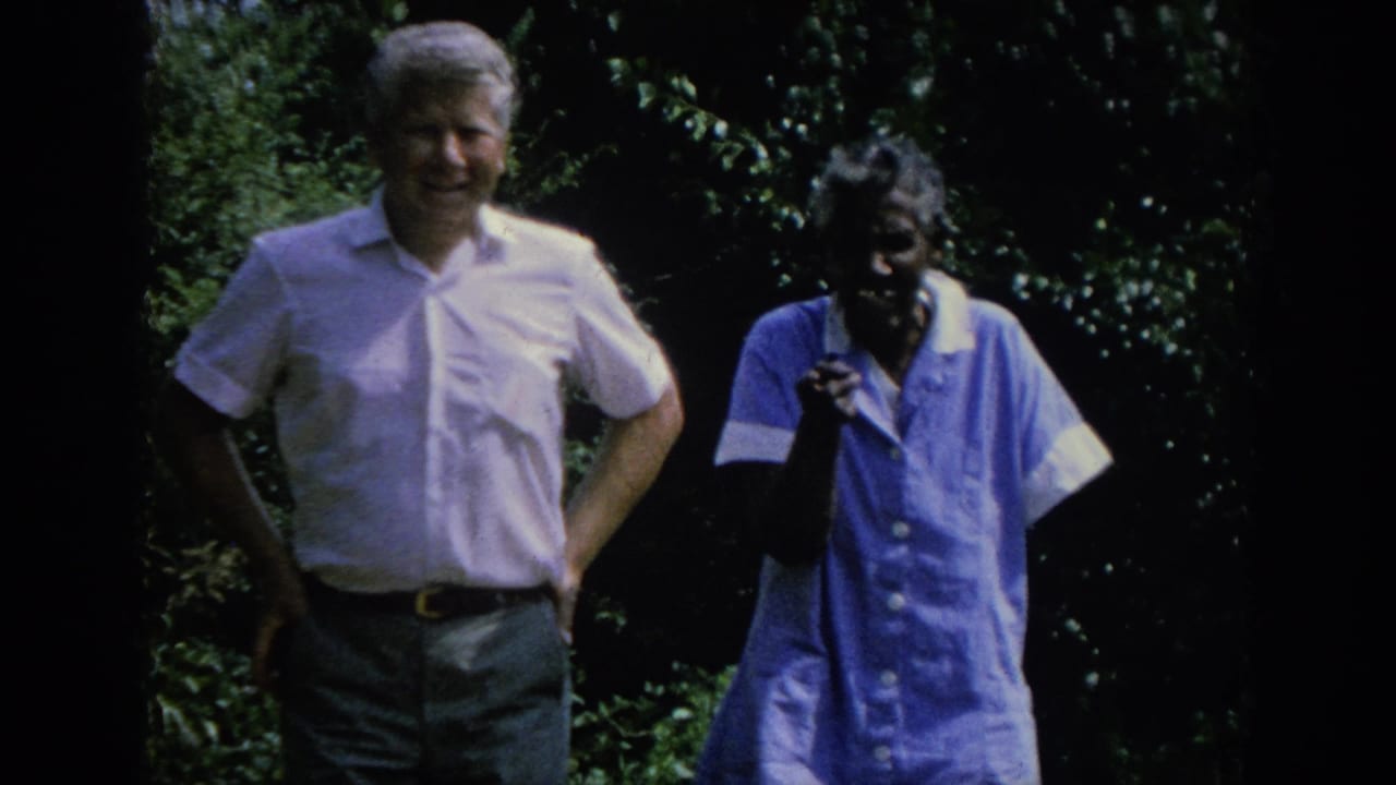 In 1962 Blainsport, Pennsylvania footage, a white man and an elderly Black woman stand together in a leafy garden area.