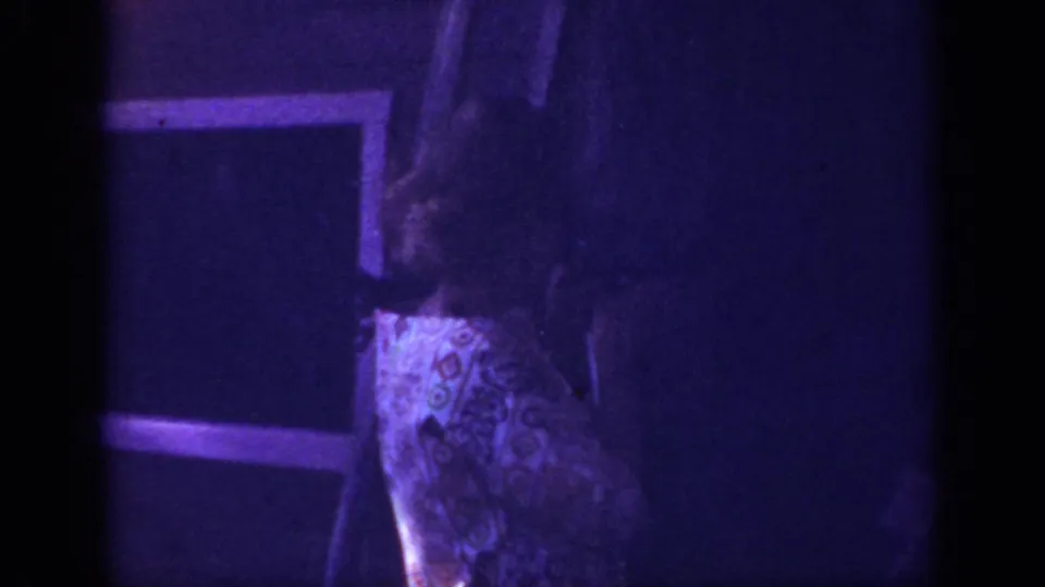 Final 1962 home-movie frame appears to show a partial person in a patterned dress inside a dark, purple-tinted interior space.