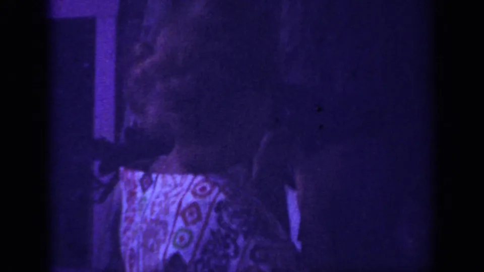 In the 1962 Blainsport footage, the woman turns beside a dark interior frame while grain and purple color shift obscure detail.