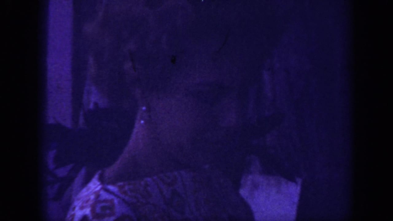 1962 Blainsport home-movie frame showing a woman close to the camera in a patterned dress, with heavy purple cast and dark gate edges.