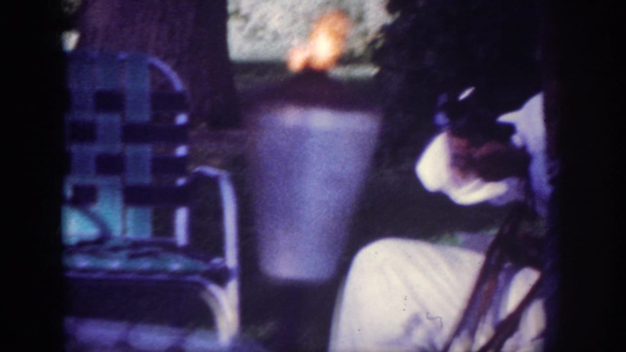 1962 Blainsport backyard frame with a small flame or torch, metal lawn chair, and a seated adult partly visible.