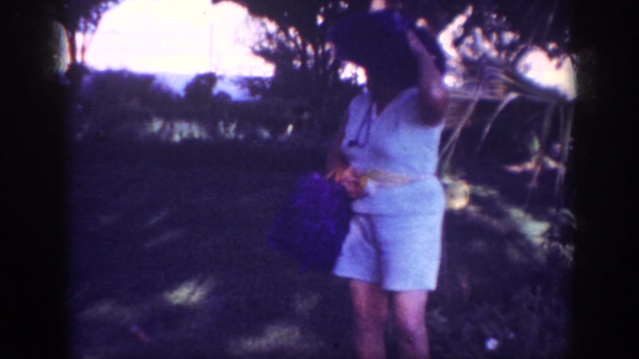 In Blainsport, Pennsylvania, 1962 home-movie footage, a woman in light clothing and a wide-brimmed hat stands in shaded grass near trees.