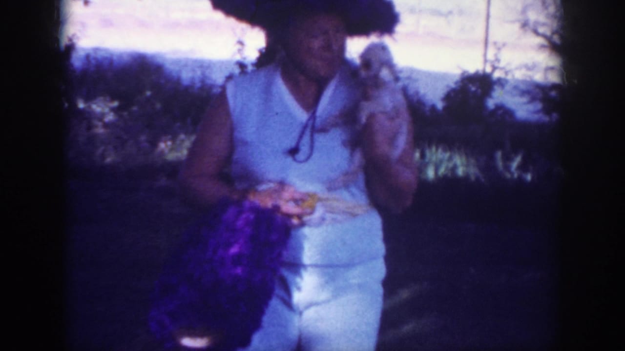 In Blainsport, Pennsylvania, 1962 home-movie footage, an elderly woman in a white sleeveless dress and large dark hat holds a small white dog.