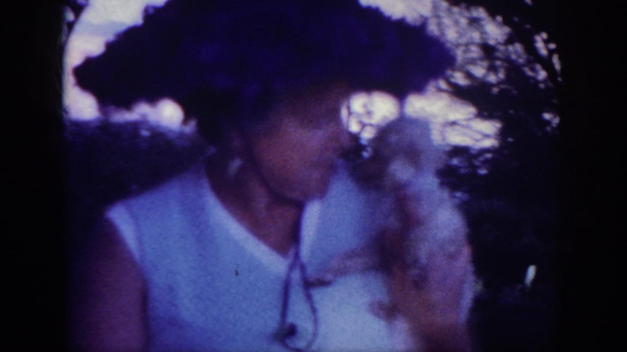 Woman in a dark hat holds a small white dog close to her face.