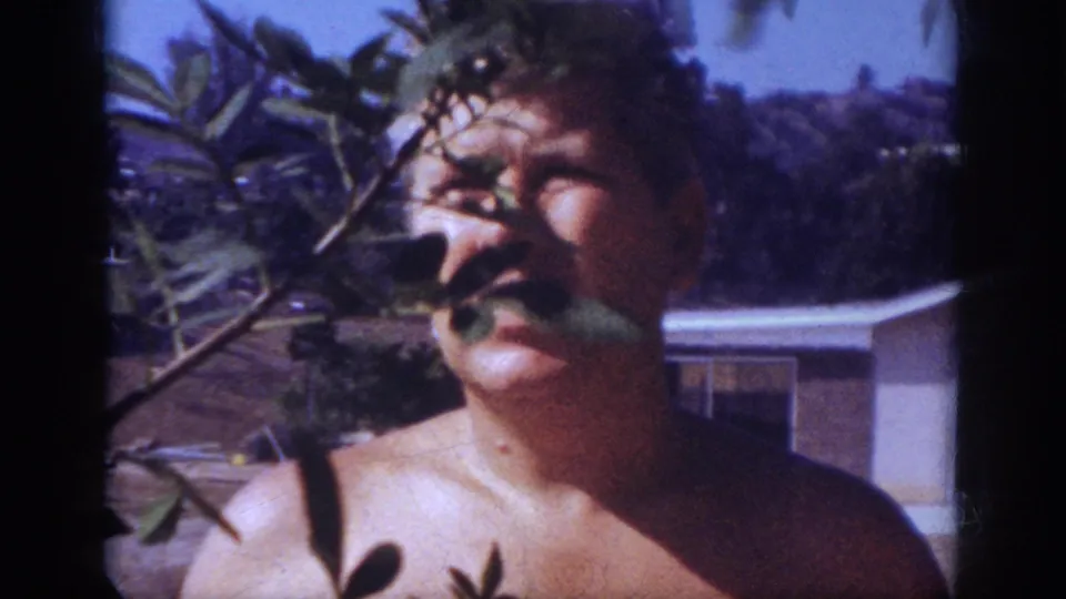 A close 8mm frame shows the man near the camera, his face partly obscured by leaves in the Blainsport patio scene.