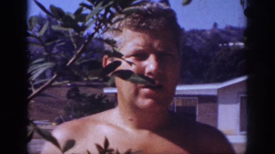 The man looks toward the camera through foreground leaves in the 1962 Blainsport home-movie footage.