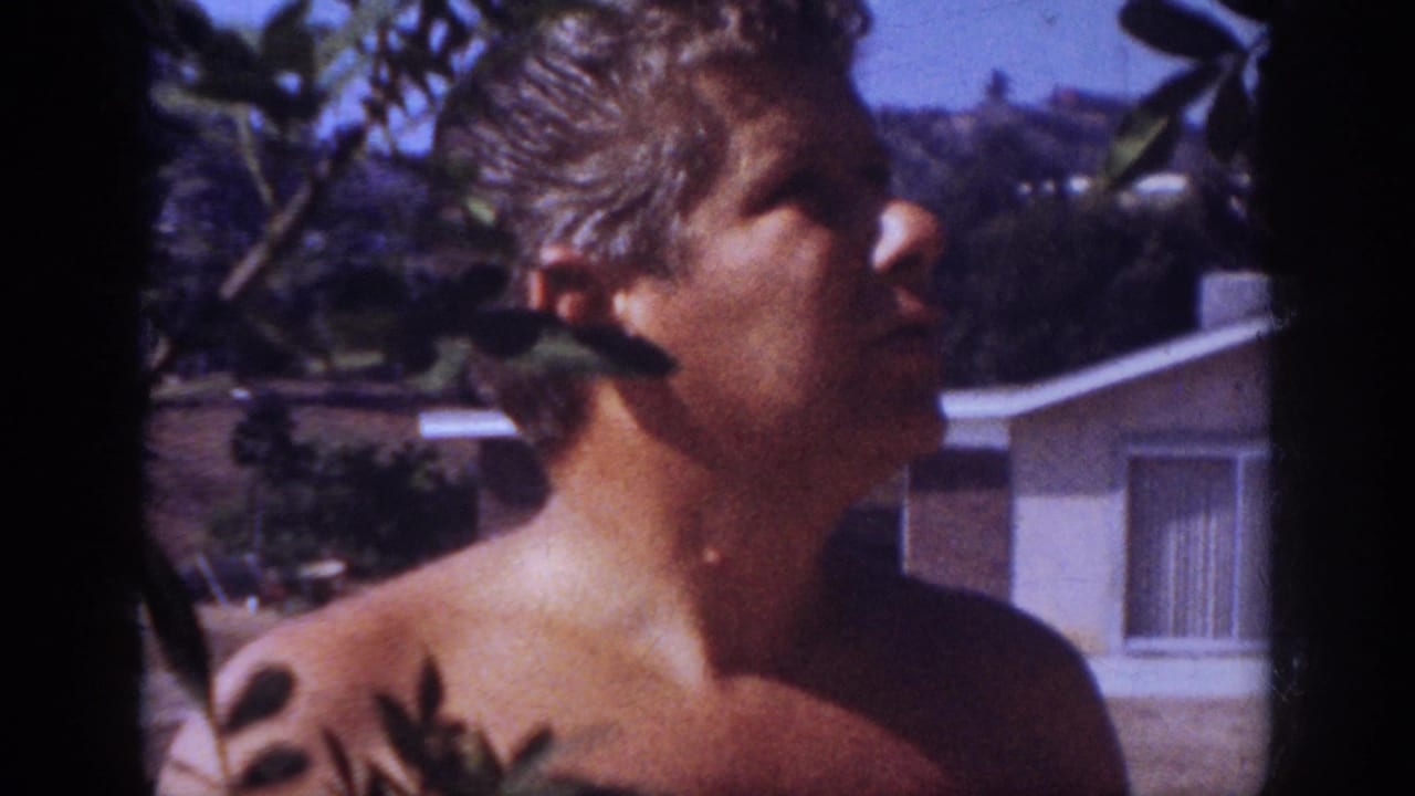 In 1962 Blainsport home-movie footage, a shirtless adult man stands outdoors near leaves and a single-story house.