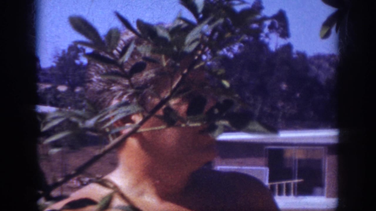 Man in profile partly hidden by a branch with a house behind him.