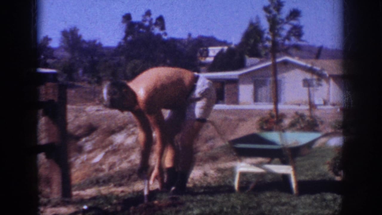 In Blainsport, Pennsylvania, a shirtless man bends over yard soil with a shovel near a young tree, wheelbarrow, lawn, and house.