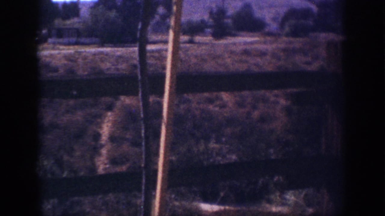 1962 Blainsport, Pennsylvania 8mm frame showing a weathered wooden fence, dry grass, shrubs, and distant low hills.