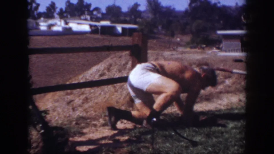 The man bends low beside the wooden fence in Blainsport, Pennsylvania, appearing to work with dirt or something at ground level.