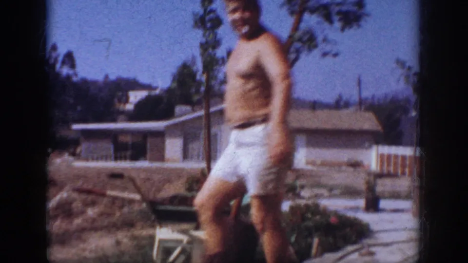 In 1962 Blainsport home-movie footage, a shirtless adult man stands in a suburban backyard during a tree-planting task.