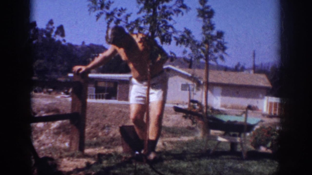 In Blainsport, Pennsylvania, 1962, a shirtless man in white shorts works near a newly planted tree in a suburban yard.