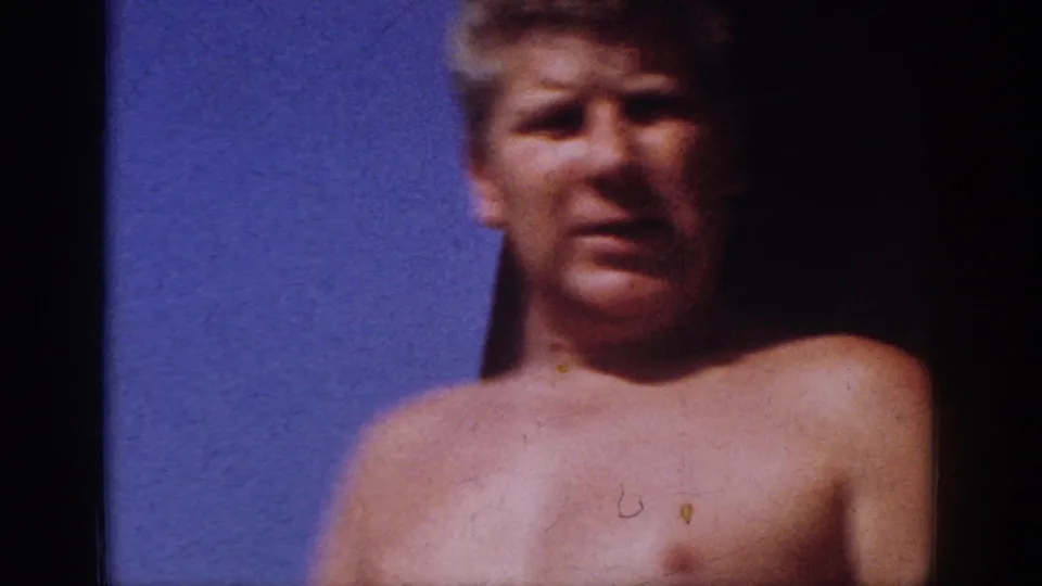 Shirtless adult man in a 1962 Blainsport home-movie frame, softly focused against blue sky with dark film edges.